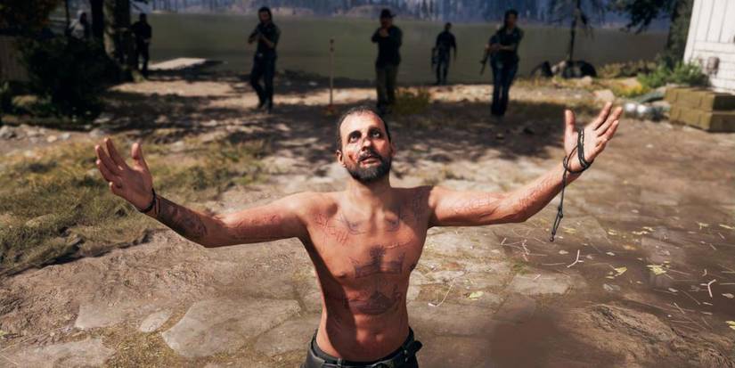 Joseph Seed raising his arms to the sky, various characters approaching from behind with guns